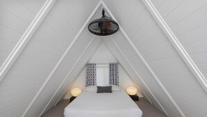 Um quarto pequeno e triangular com uma cama, duas luminárias de cabeceira e um ventilador de teto.