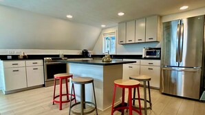 Uma cozinha moderna com uma ilha central, eletrodomésticos de aço inoxidável e banquetas vermelhas.