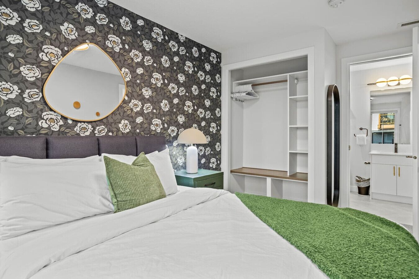 Une chambre à coucher comprenant un lit, une table de chevet, un miroir, une armoire et une salle de bain avec un miroir et un lavabo.
