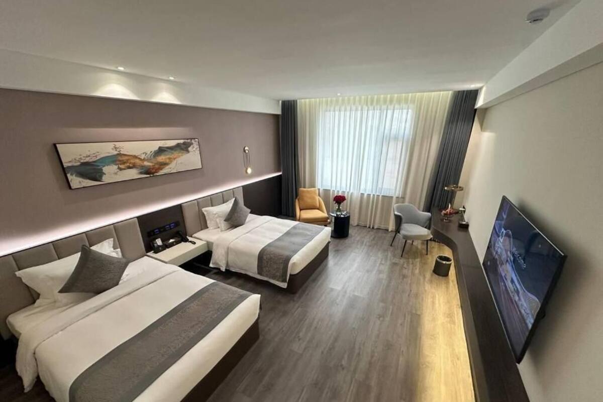 Ein Hotelzimmer mit zwei Betten, einem Schreibtisch, einem Sessel, einem Fernseher und einem großen Fenster mit Vorhängen.