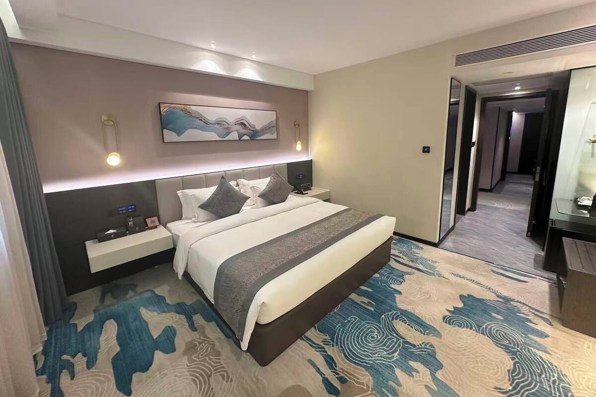 Ein modernes Hotelzimmer mit einem großen Bett, einem Nachttisch, einem Wandbild und einem Teppich mit Wellenmuster.
