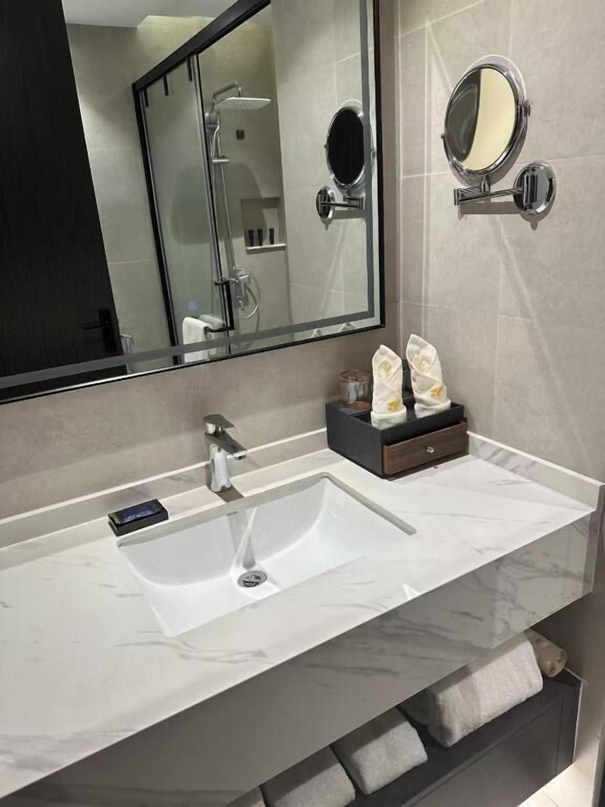 A modern bathroom with a large mirror, a sink, and a shower.