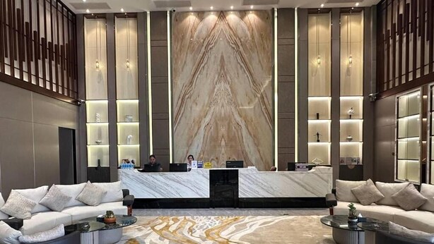 Eine moderne Lobby mit einem Marmor-Empfangstresen, zwei Sofas, einem gemusterten Teppich und einer Wandverkleidung.