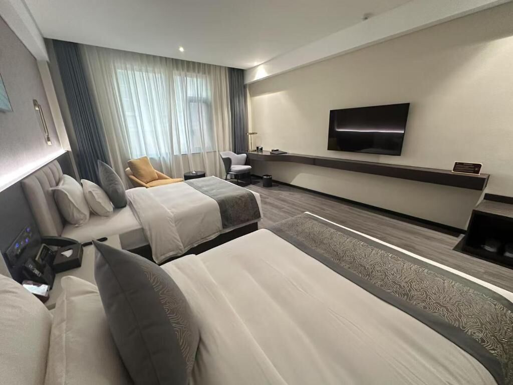 Een hotelkamer met twee bedden, een aan de muur bevestigde televisie, een bureau en een stoel.