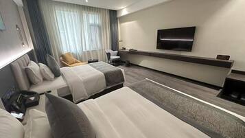 Een hotelkamer met twee bedden, een aan de muur bevestigde televisie, een bureau en een stoel.