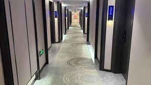 Ein Hotelkorridor mit einem gemusterten Teppich, Türen auf beiden Seiten und eingelassener Beleuchtung.