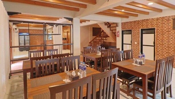 A dining area with wooden tables and chairs, a brick wall, and a staircase. - ye layeku boutique hotel pvt ltd (Kathmandu)