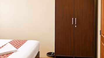 Een slaapkamer met een bed, een houten garderobe en een kleine prullenbak.