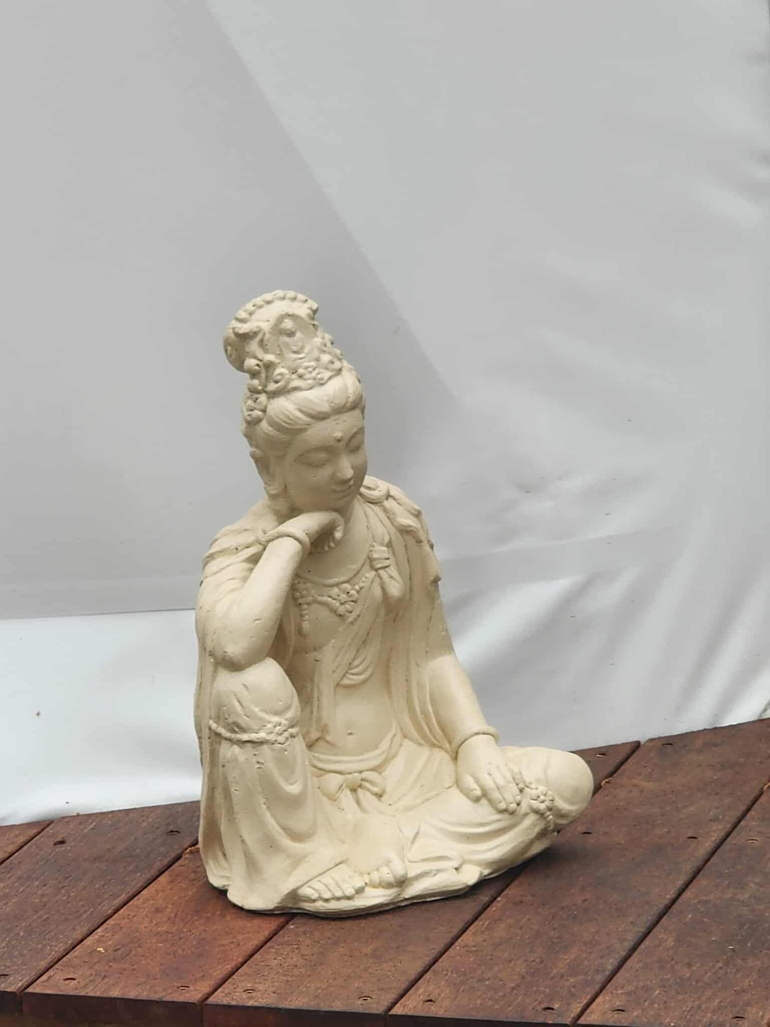 Una estatua blanca de una figura sentada sobre una plataforma de madera.