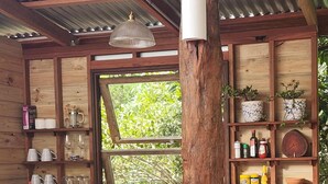 A rustic kitchen with wooden shelves, a window, and a wooden pillar. - Solara Dome Off Grid Luxury and Stillness at Shanlyn Farm (Traveston)
