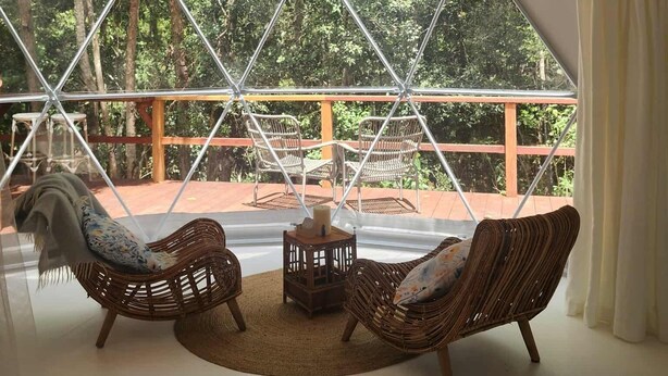 A tented room with wicker furniture, a chandelier, and a view of trees. - Solara Dome Off Grid Luxury and Stillness at Shanlyn Farm (Traveston)
