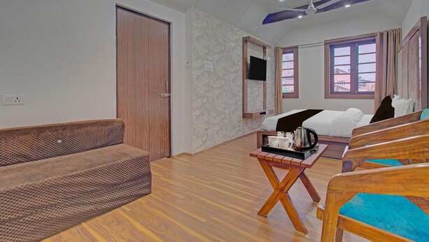 A hotel room with a wooden floor, a sofa, a bed, a TV, and a window with curtains. - Classic Main Street Inn (Srinagar)