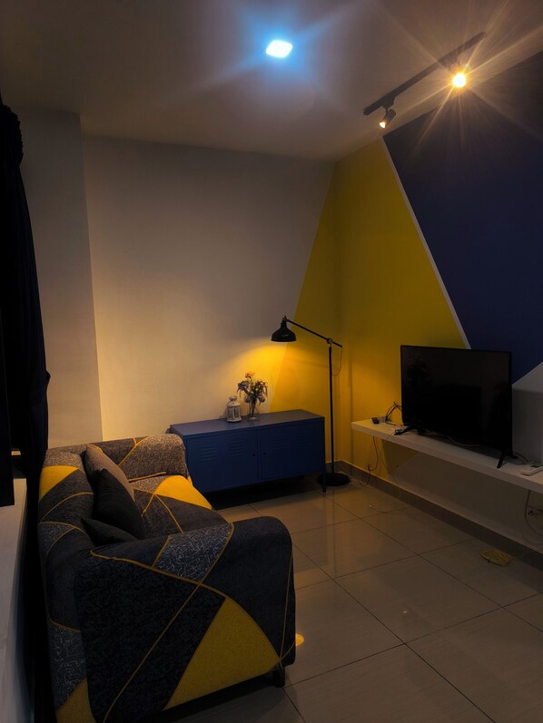 Una sala de estar moderna con un sofá, un televisor sobre un mueble, una lámpara y un aparador azul.