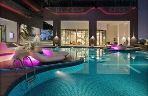 Un área de piscina interior moderna con diseño curvo, asientos junto a la piscina y vistas del interior del edificio.