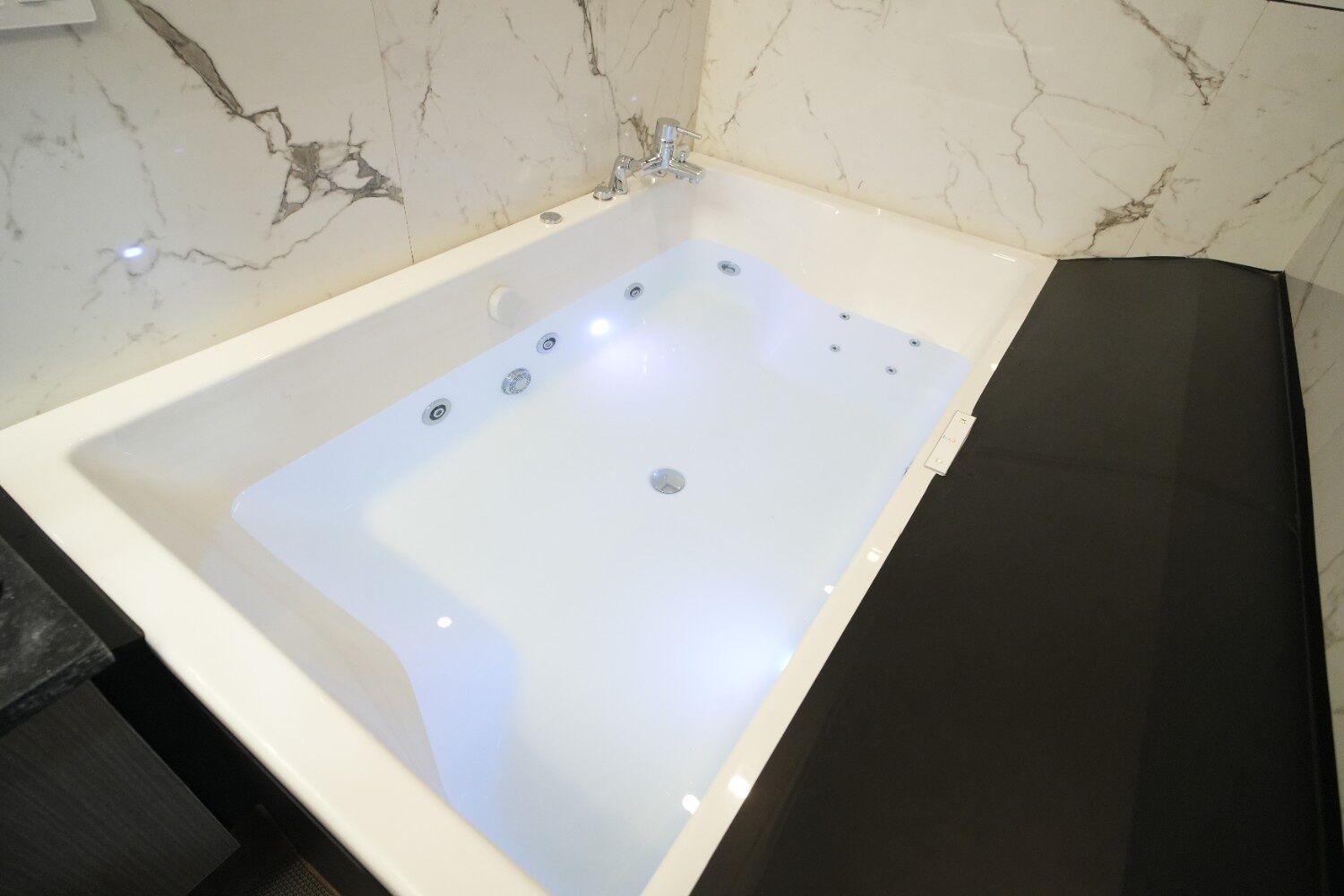 A modern bathroom with a marble wall, a white bathtub, and a black countertop.