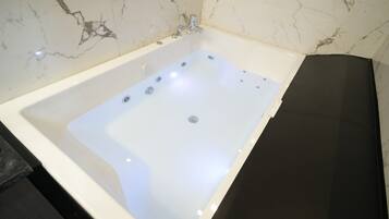 A modern bathroom with a marble wall, a white bathtub, and a black countertop.