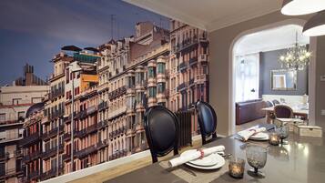 Een eetgedeelte met een tafel voor vier personen, een stadsgezicht muurschildering aan de muur, en zicht op een woonkamer.