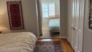 Una camera da letto con un letto, un comodino, un tappeto rosso e bianco e una ventola a soffitto.