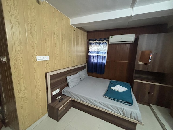 A compact bedroom with a bed, a small bedside table, a wardrobe, and an air conditioning unit. - New Hotel Tuk Tuk Palace (Ranchi)