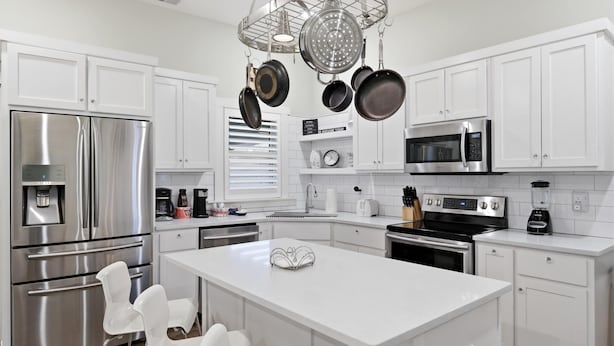 A modern kitchen with white cabinets, stainless steel appliances, and hanging pots.