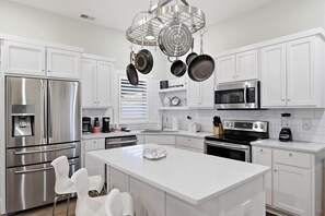 A modern kitchen with white cabinets, stainless steel appliances, and hanging pots. - Bright & cozy Louisville home w/ private backyard (Louisville)