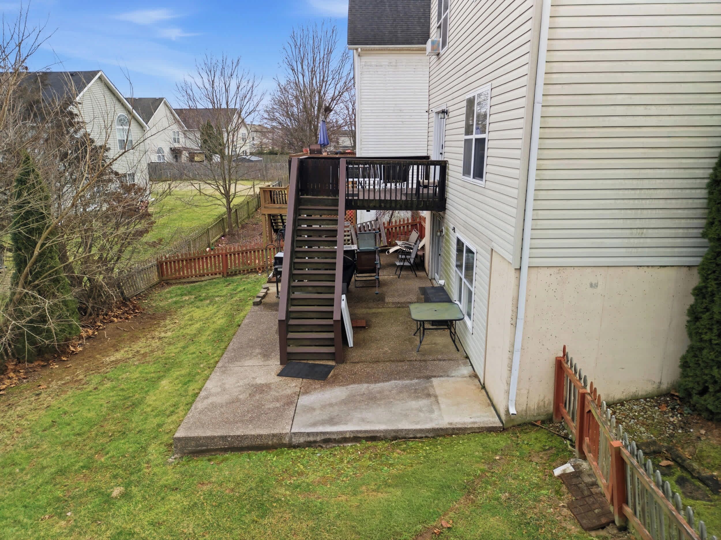A backyard with a wooden staircase leading to a deck, a patio table, and a barbecue grill.