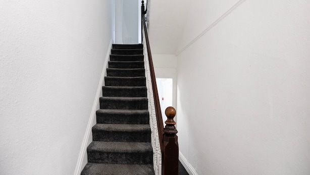 A staircase with dark carpeted steps and a wooden handrail with a rounded top. - Standard Quad Room (Salford)
