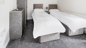 A modern hotel room with two single beds, a grey wardrobe, and a small bedside table with a lamp. - Standard Quad Room (Salford)