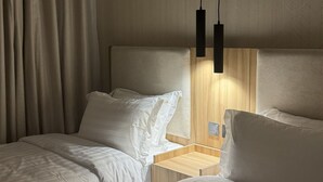 Ein Hotelzimmer mit zwei Betten, einem Holzkopfteil, einem Nachttisch und einer Pendelleuchte.