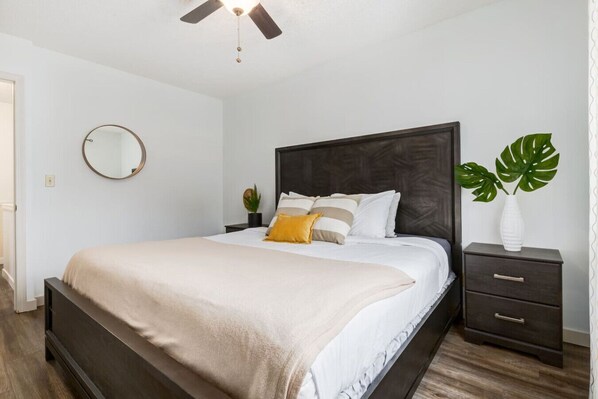 A bedroom with a bed, a nightstand, a mirror, and a plant.