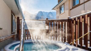 Un jacuzzi rodeado de nieve, con una valla de madera y vistas a la montaña al fondo.