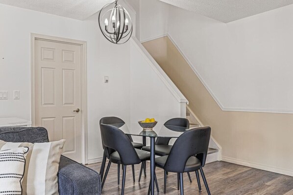 A dining area with a table and four chairs, a chandelier, a staircase, and a door.