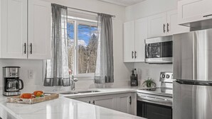 Una cocina moderna con armarios blancos, electrodomésticos de acero inoxidable, una cafetera y una ventana con cortinas.