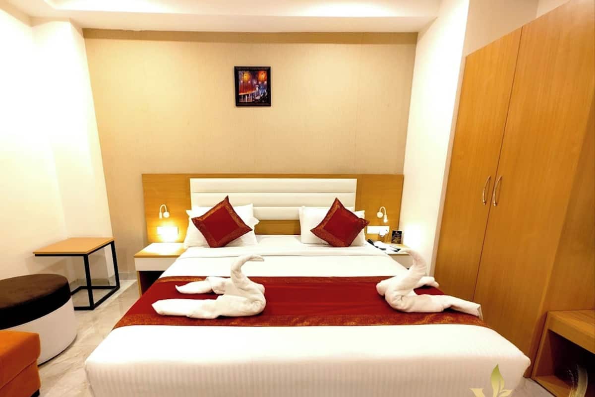 Una habitación de hotel con una cama grande, dos mesitas de noche, un armario de madera y una pequeña mesa.