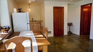 Un'area pranzo con un tavolo e sedie in legno, un frigorifero bianco, una cucina con mobili in legno e una porta in legno.