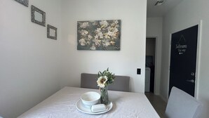 Un coin repas avec une table dressée pour deux personnes, un vase rempli de fleurs et un tableau accroché au mur.