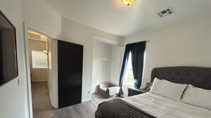 Une chambre à coucher comprenant un lit, une table de chevet, une fenêtre avec des rideaux et une porte donnant sur une autre pièce.