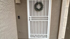 Une porte blanche ornée d’une guirlande décorative et d’un paillasson sur lequel est écrit « Bonjour » devant l’entrée.