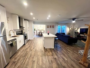 A modern kitchen with white cabinets, a central island, and a dining area with a blue sofa. - Stylish 4BR Retreat in Denton | Sleeps 10 UNT TWU (Denton)