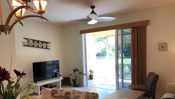 Uma sala de estar com televisão de tela plana, um sofá, uma poltrona e um ventilador de teto.