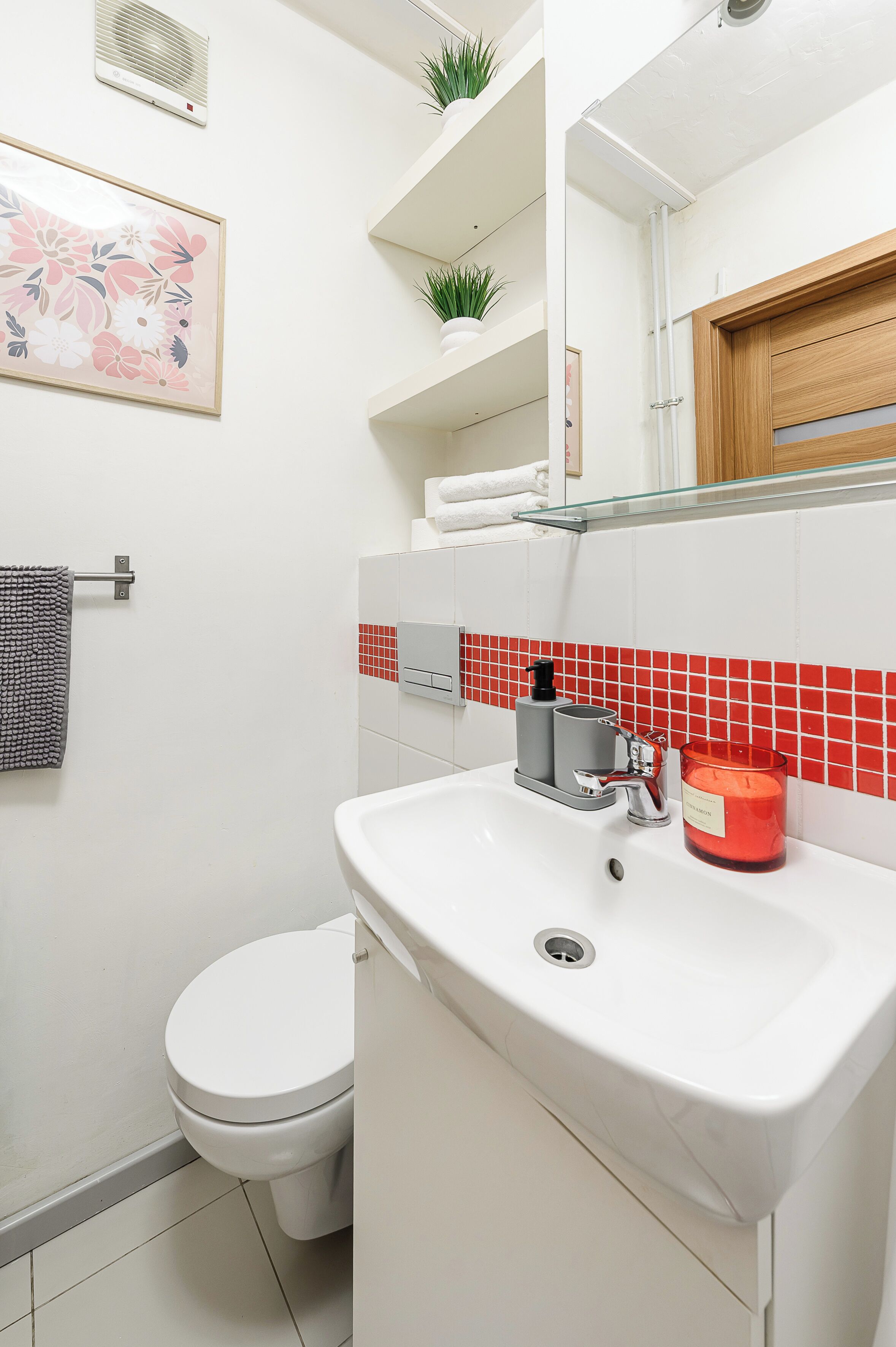 Un baño con un inodoro blanco, un lavamanos con dispensador de jabón rojo y un espejo sobre el lavamanos.