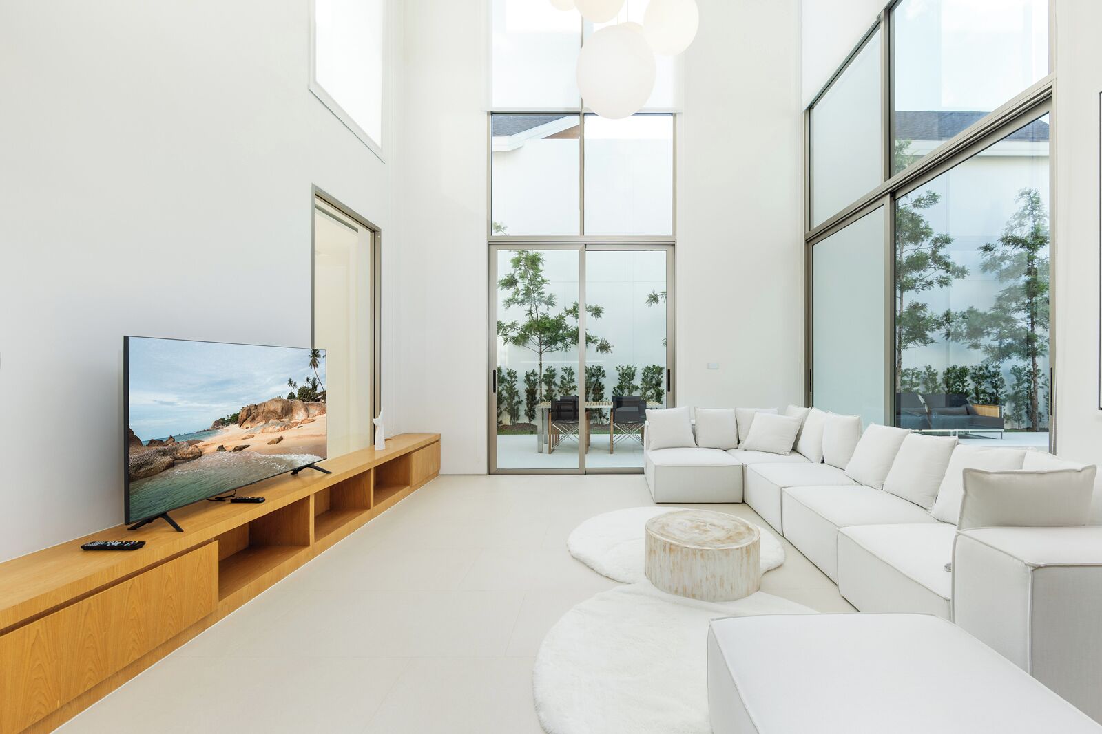 A modern living room with a large flat-screen TV, a white sectional sofa, and a wooden entertainment unit.