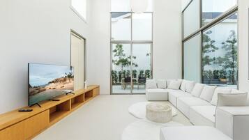 A modern living room with a large flat-screen TV, a white sectional sofa, and a wooden entertainment unit.