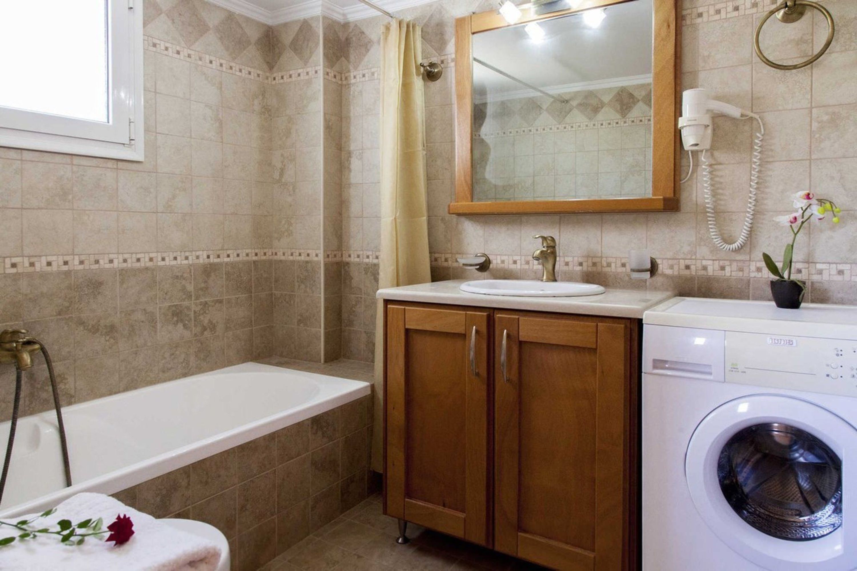 A bathroom with a bathtub, a sink, a mirror, a hairdryer, and a washing machine.