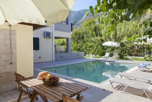 A poolside area with a table, chairs, and umbrellas. - Azalea Villas (Lefkada)