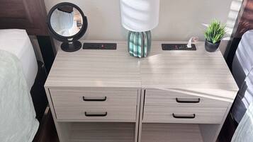 A modern bedroom with a wooden dresser, a round mirror, a lamp, and a small potted plant.