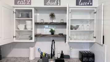 A kitchen with open cabinets displaying dishes, a sink with a faucet, and a countertop with a coffee maker and toaster.