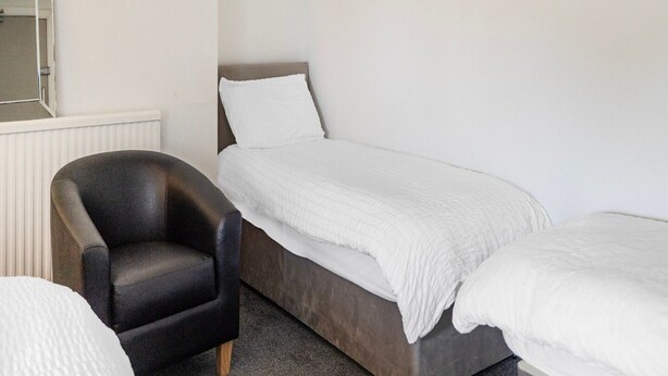 A single bed with a white duvet, a black leather chair, and a white radiator. - Standard Double Room (Salford)