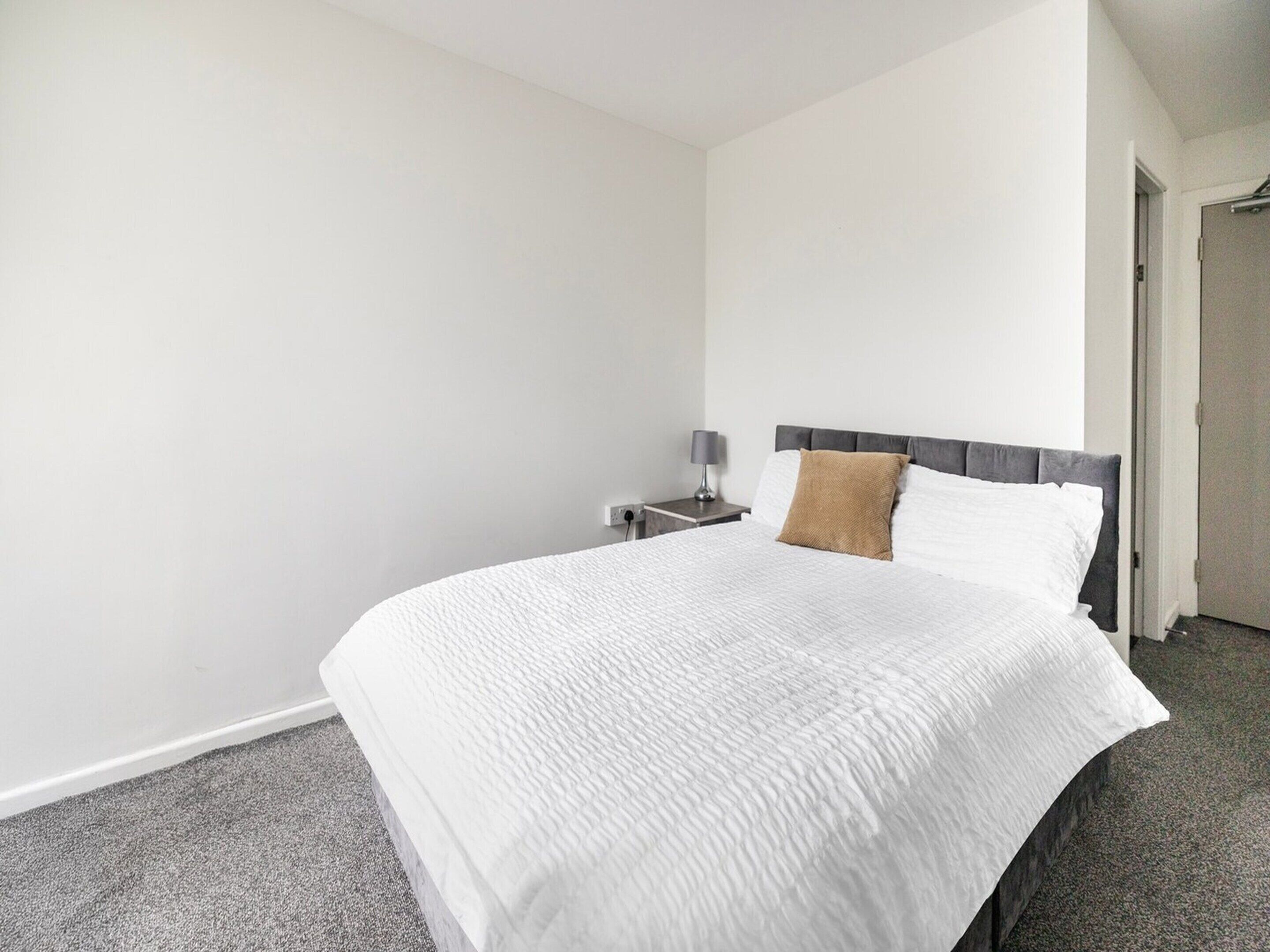 A hotel room with a large bed, a nightstand, a lamp, and a door leading to another room.