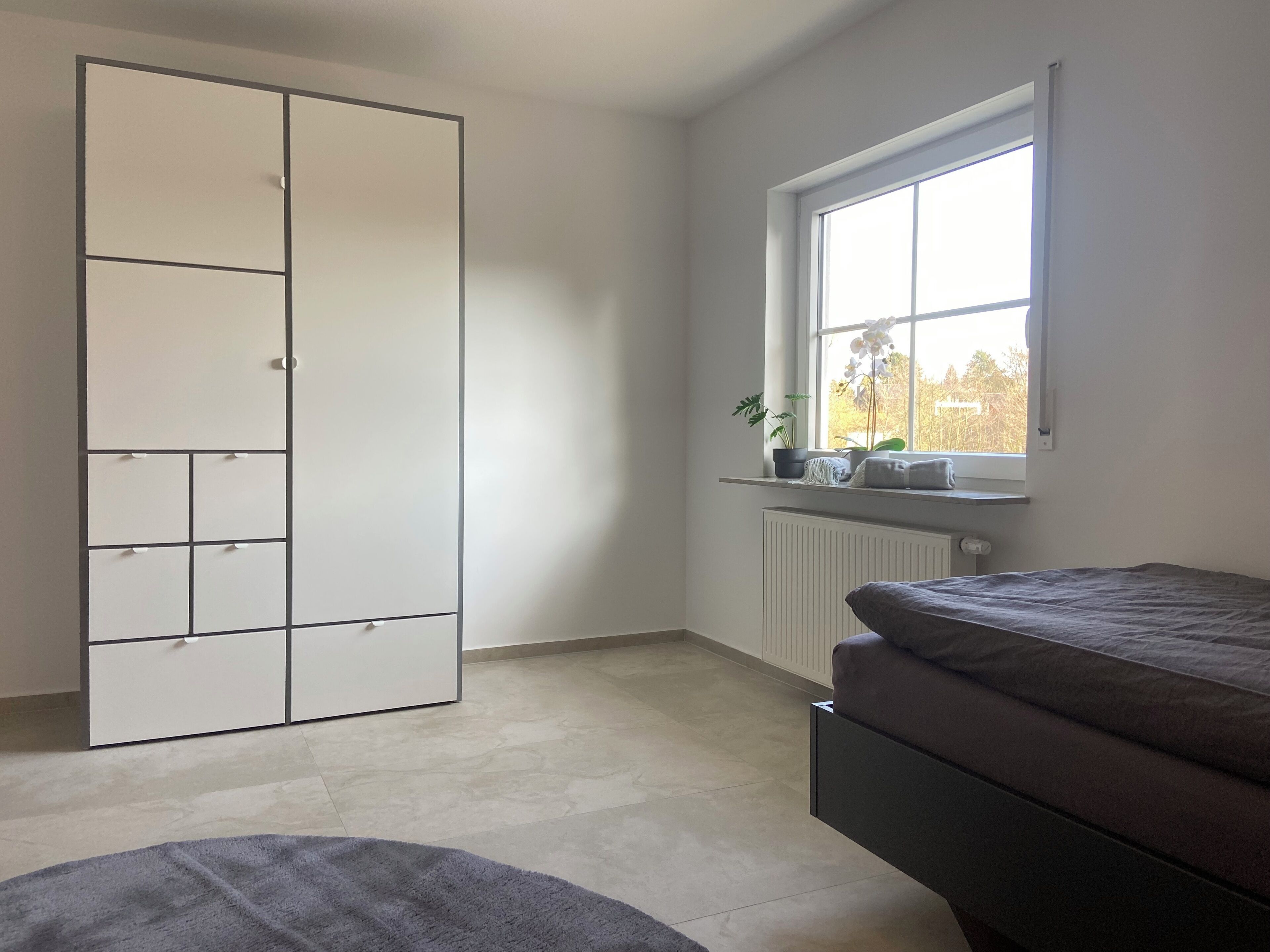 Ein Schlafzimmer mit Bett, Kleiderschrank, Fenster mit Blick und Heizkörper.